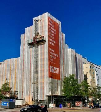 Suojapeitteisiin verhottu kerrostalo telineineen, julkisivussa Constin oranssi mainoslakana